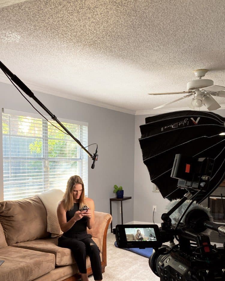 Nichole on a couch between takes, camera and light set up in front of her