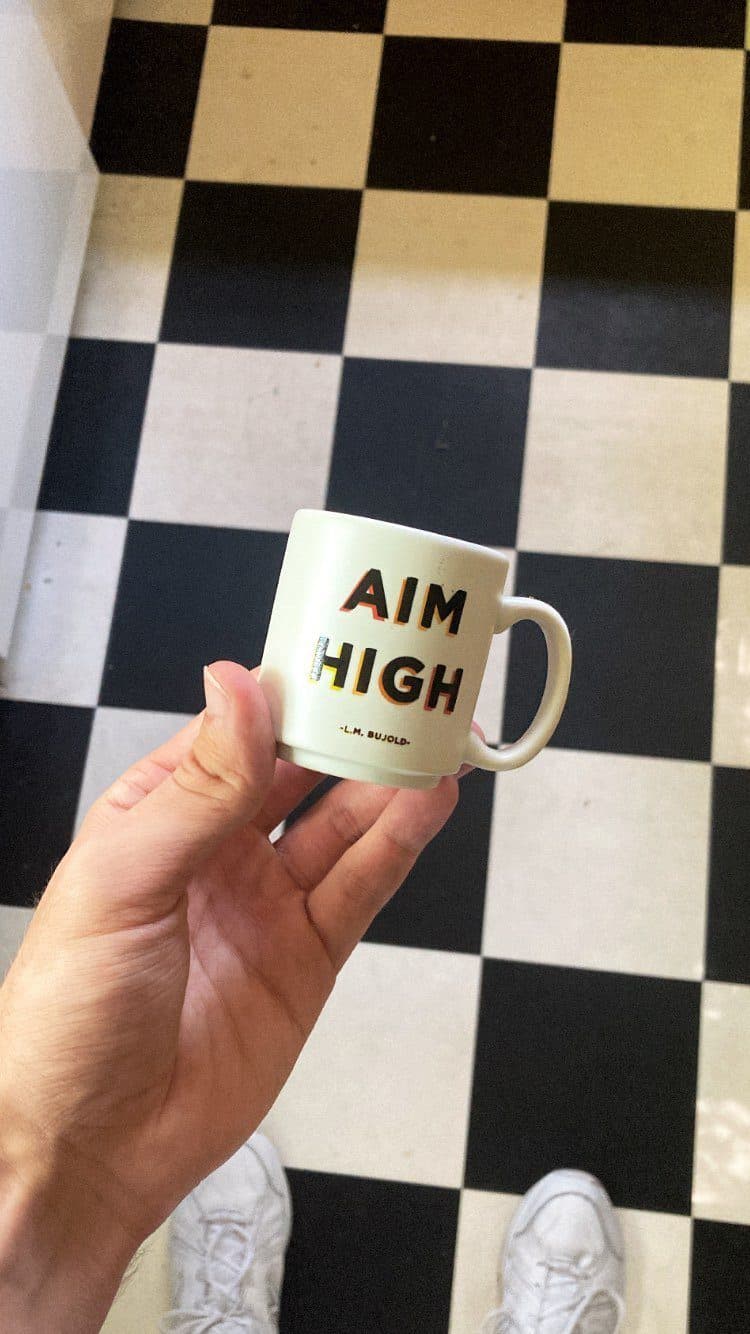 A coffee mug that says Aim High on a checkered floor