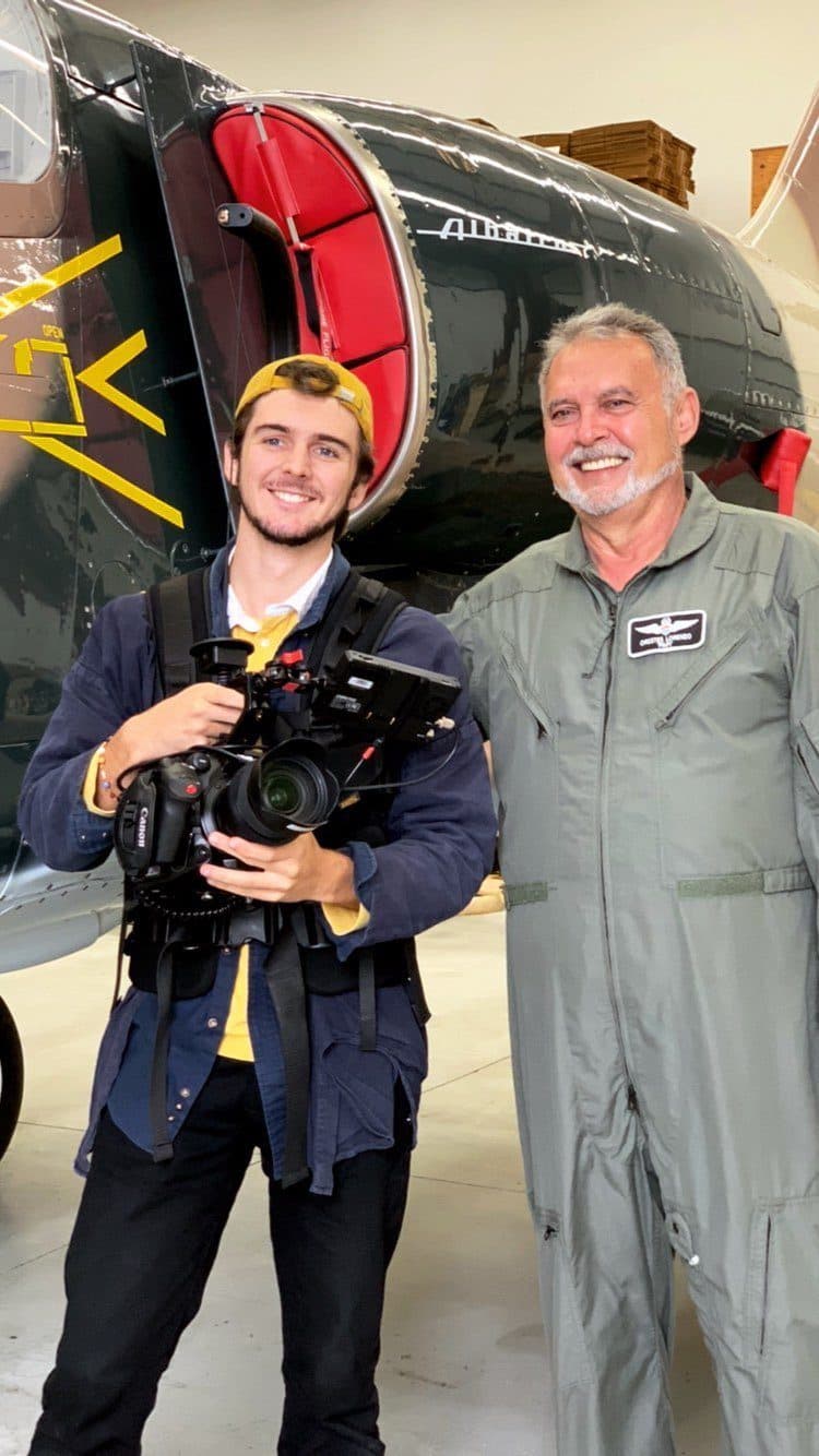Caleb holding a camera next to a pilot in a flight suit