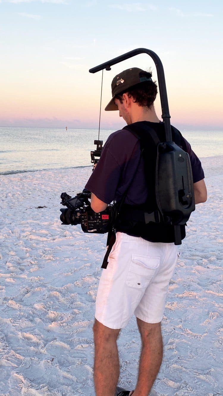 Caleb on the beach at sunset with a camera rig on his shoulder